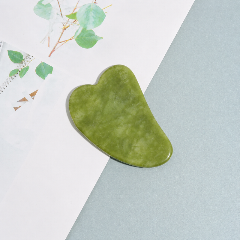 Green gua sha tool on a light blue and white background